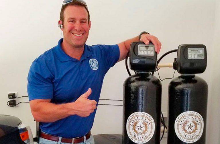 Technician giving thumbs up beside water softener tanks