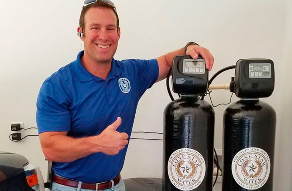 Technician giving thumbs up beside water softener tanks
