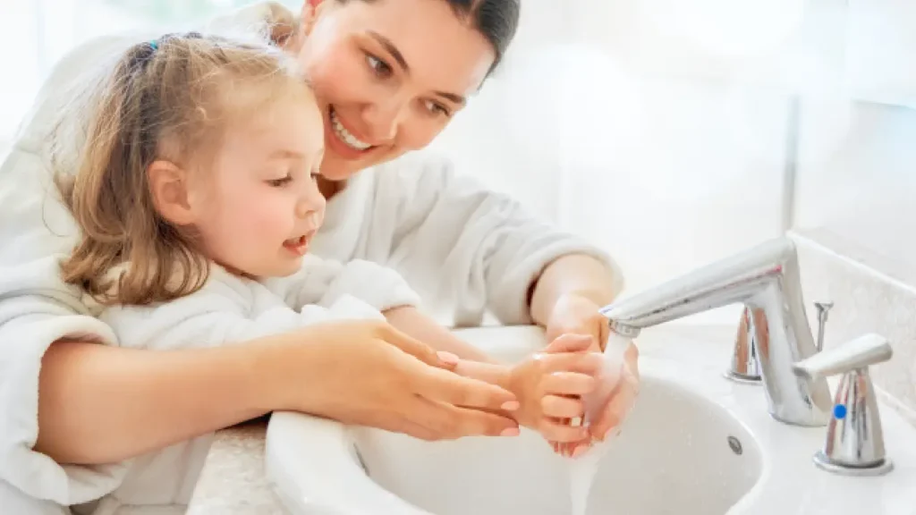 mother helps her toddler wash hands in the kitchen sink